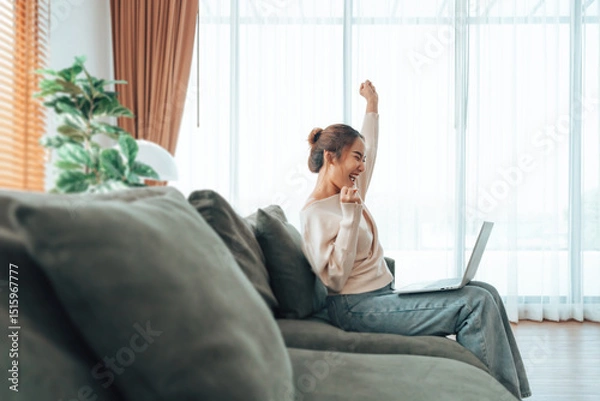 Fototapeta Funny euphoric young asian woman celebrating winning or getting ecommerce shopping offer on computer laptop. Excited happy girl winner looking at notebook celebrating success