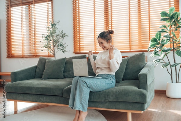 Fototapeta Funny euphoric young asian woman celebrating winning or getting ecommerce shopping offer on computer laptop. Excited happy girl winner looking at notebook celebrating success