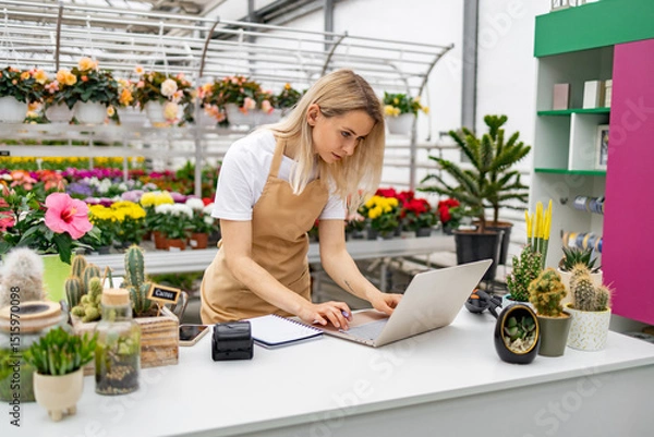 Obraz A Caucasian woman works on a laptop at a table in a flower shop surrounded by colorful plants and flowers.