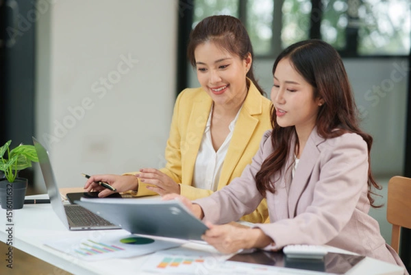 Fototapeta Group of two Asian businesswomen using laptops and tablets having a meeting about working together.