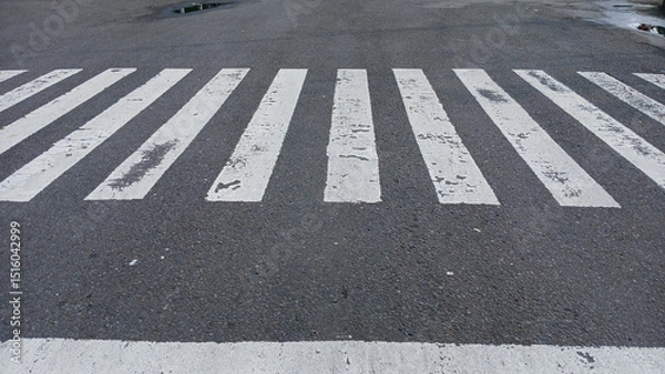Obraz Close-up of a worn pedestrian crossing on an asphalt road, showing urban textures and details of everyday street life. Concept of transportation or city infrastructure.