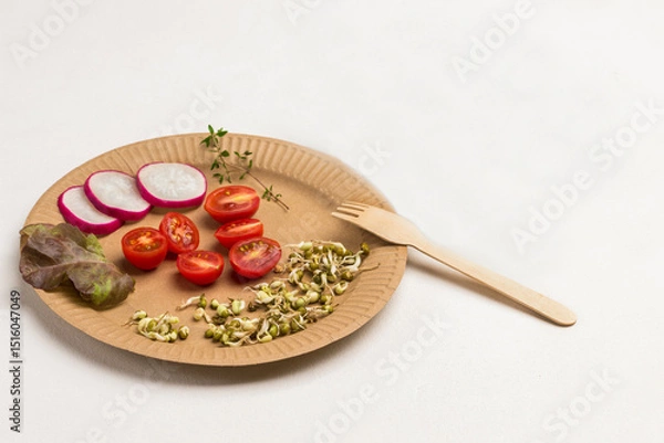Fototapeta Germinated mung bean sprouts, halved tomato and slices of radish on cardboard disposable plate. Fork on plate.