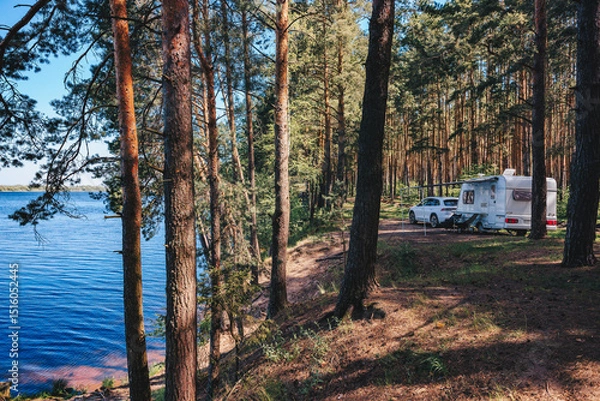 Fototapeta Caravan RV parked on the beach under a trees facing blue sea, lake or river. Family traveling with motorhome. Travelers on an active family vacation.