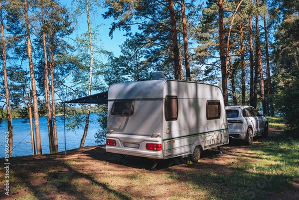 Fototapeta Caravan RV parked on the beach under a trees facing blue sea, lake or river. Family traveling with motorhome. Travelers on an active family vacation.