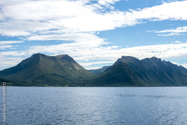 Fototapeta High mountains of Gjevenesstranda nature reserve, along Storfjord in Norway, near Solavagen, under a bright blue sky with scattered clouds seen from the water on a sunny day