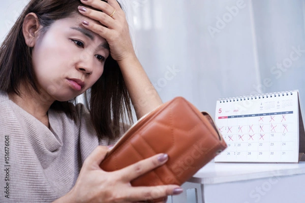 Obraz Asian woman feeling stressed while checking her empty wallet, worried about running out of money before the end of the month struggling with being broke and unable to cover expenses