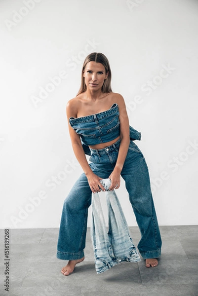 Fototapeta Stylish model poses in denim outfit with casual confidence in minimalistic studio setting