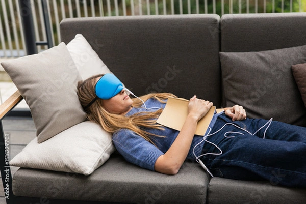 Fototapeta Woman sleeping with temperature controlled sleep mask and book on chest