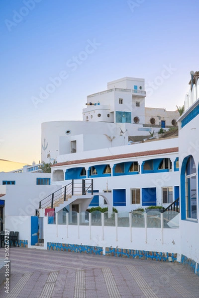 Fototapeta Coastal promenade in Sidi Ifni showcasing blue and white architecture at sunset