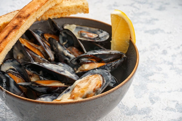 Obraz Mussels in Dor Blue sauce in a bowl with lemon and croutons, close-up.