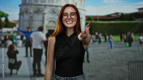 Fototapeta Woman smiling extends hand with pisa tower in background surrounded by visitors in outdoor setting in italy.