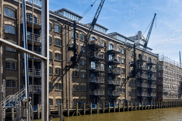 Fototapeta London, UK,  7 May 2025,  New Concordia Wharf. Historic Riverside Buildings with Cranes in London.