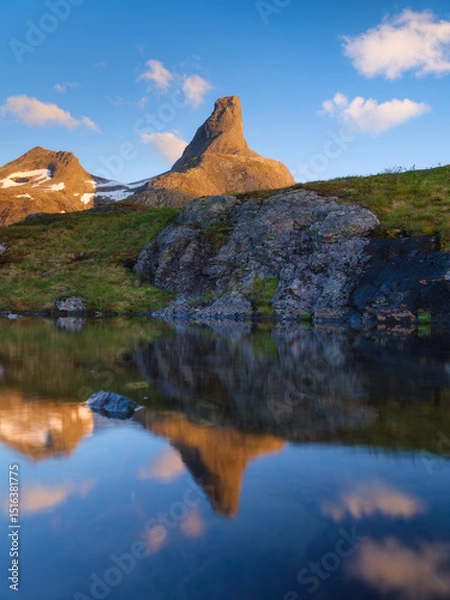 Fototapeta Norway. Mountain landscape. View of a high mountain in a valley. Huge sharp rocks and reflection on the water surface. Landscape in summer time. A place for trekking.
