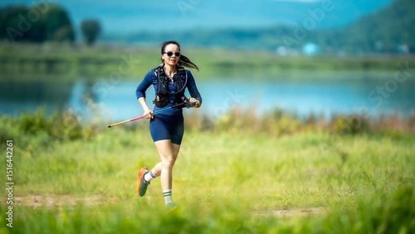 Fototapeta A woman is running in a field with a stick in her hand. The stick is red and blue