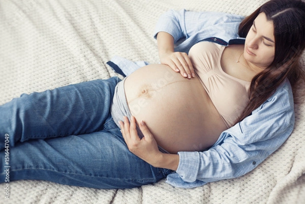 Obraz A pregnant woman is seen resting comfortably on bed. She appears content and serene, enjoying a quiet moment