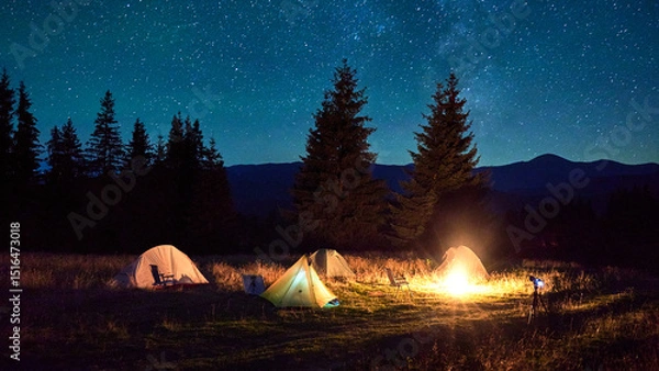 Fototapeta Several tents around glowing campfire on grassy clearing under starry sky. Warm light of campfire illuminates scene, creating cozy and serene night camping atmosphere in the mountains.