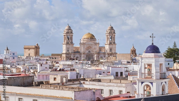 Fototapeta A stunning view of Cádiz Cathedral with its iconic golden dome rising above the traditional whitewashed buildings of the old town, under a bright blue sky.