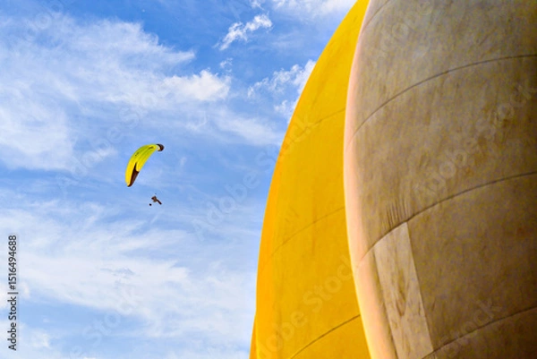 Obraz Paragliding in a blue sky with clouds and a yellow hot air balloon in the background.