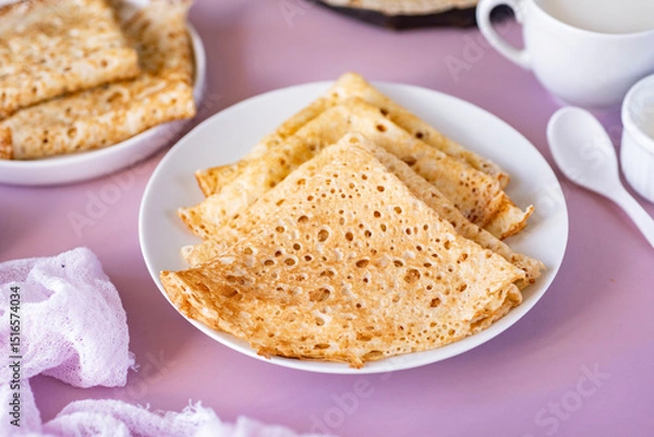 Fototapeta Delicious homemade breakfast: thin large pancakes on a beautiful white plate on a pink background. Thin pancakes for dessert. View from above. Close-up