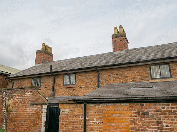 Fototapeta Rustic brick house terraced with chimney stacks under a cloudy sky.