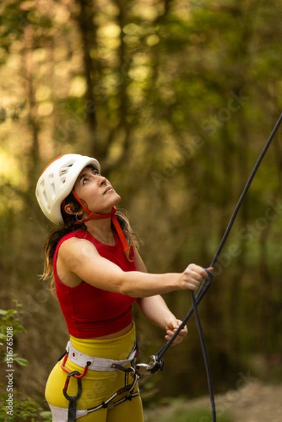 Obraz A woman in a red top and yellow pants is climbing a rope