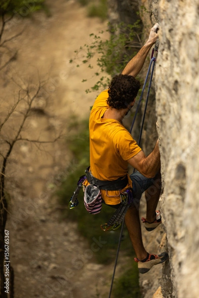 Obraz A man in a yellow shirt is climbing a rock wall