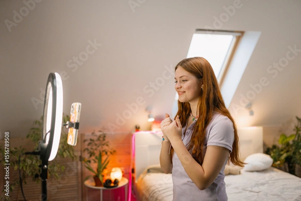 Obraz The girl shoots a video blog on her mobile phone. She stands in front of a ring lamp and dances
