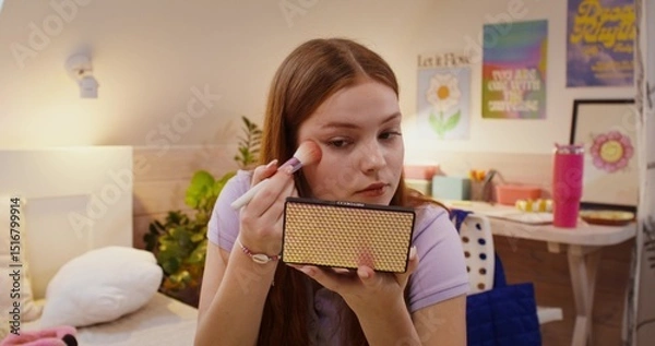Obraz A girl does her makeup while sitting on the bed. She puts blush on her face with a brush.