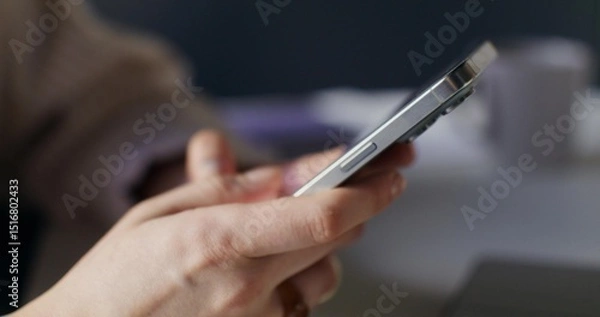 Obraz A woman uses a mobile phone while sitting indoors. Close-up of her hands, unrecognizable person