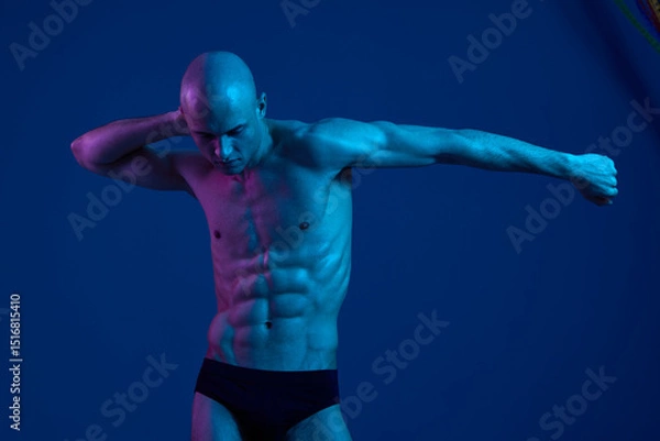 Fototapeta Athletic man posing in dramatic light, showcasing defined muscles. The image features a blend of blue tones, highlighting strength and vitality in a striking manner.