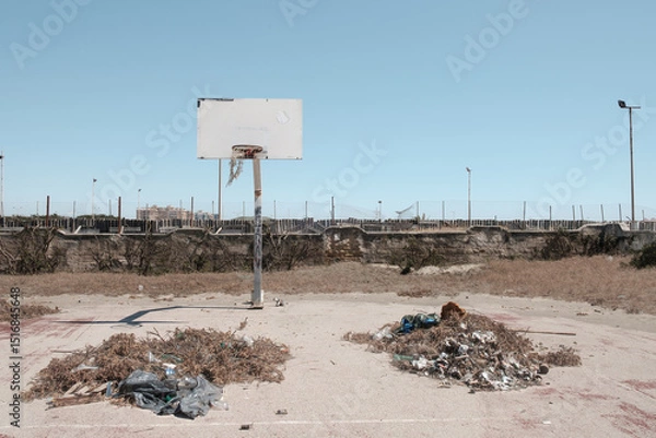 Fototapeta An abandoned basketball court, in a state of decay, with piles of rubbish and brushwood in the center of the field.