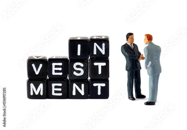 Fototapeta Two miniature businessmen figurines shake hands beside black letter blocks spelling "INVESTMENT" on a white background. This scene symbolizes a business deal or partnership in the context of financial