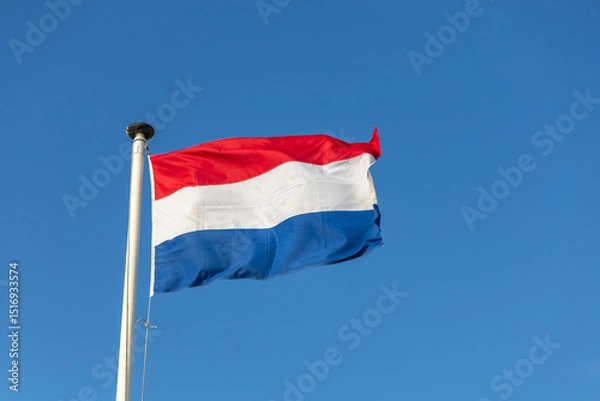 Obraz The vibrant red, white, and blue flag of the Netherlands proudly waves against a clear, azure sky, symbolizing national pride and freedom.