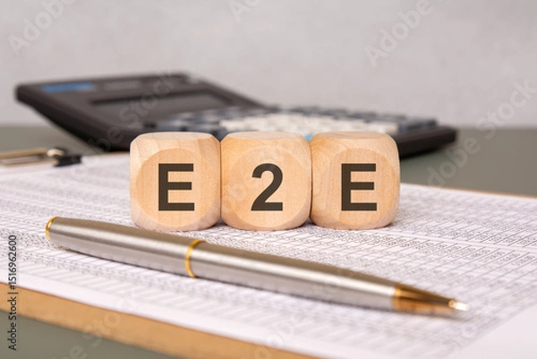 Obraz Wooden cubes spelling E2E on a spreadsheet with a pen and calculator in the background.