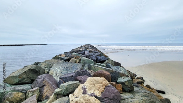 Fototapeta Narrow strip of green and brown rocks stretching into Pacific ocean at Point Medanos Jetty separating South Mission beach from entrance channel to the bay area, San Diego, California