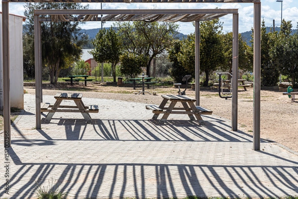 Fototapeta Two Empty gray wooden tables on the green plants background with a pergola