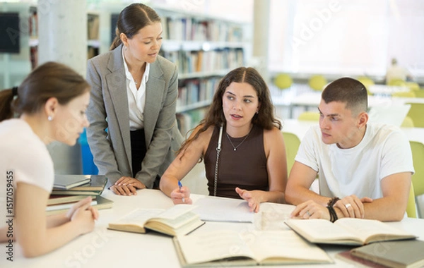Obraz Group of students talking, reading books and taking notes at table in library