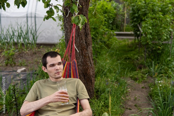 Fototapeta A man with a beer glass lies in a hammock