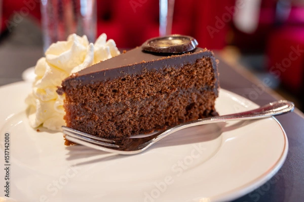 Obraz Piece of famous Sachertorte chocolate cake with apricot jam of Austrian origin served with whipped cream in old classic cafe-restaurant in Vienna