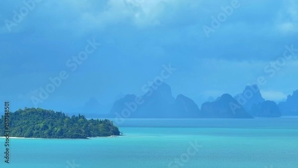 Obraz A dramatic aerial view of mountains in the distance, covered in mist and rain clouds, with the turquoise ocean beneath, creating a stunning and atmospheric coastal storm scene. Phuket, Thailand.
