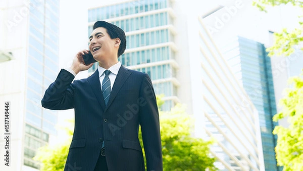 Fototapeta 新緑の街でスマホで通話する男性ビジネスパーソン