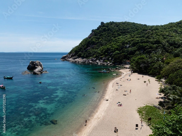 Fototapeta Sandy beach featuring turquoise water and surrounded by vibrant forested hills, with a few small boats in view. Thailand, Koh Tao.