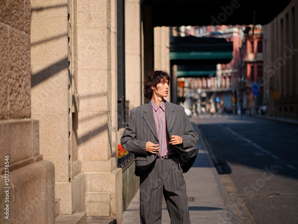 Fototapeta Portrait of handsome Chinese young man wearing gray suit posing in the street, young guy with black curly hair with urban background. Male fashion, cool Asian young man lifestyle.
