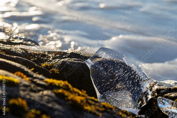 Fototapeta Close-up of a piece of transparent ice on a rock by a frozen lake on a sunny day in the winter. Focus on the foreground.