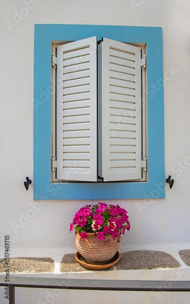 Fototapeta window surrounded in blue  with closed shutters of a house with white facade in Greece