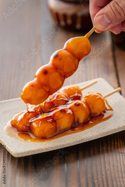 Fototapeta A close-up of traditional Japanese mitarashi dango—skewered rice dumplings grilled to perfection and coated with a glossy, sweet soy sauce glaze. The caramelized surface and rich glaze highlight the a