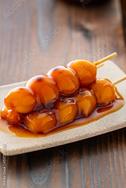 Fototapeta A close-up of traditional Japanese mitarashi dango—skewered rice dumplings grilled to perfection and coated with a glossy, sweet soy sauce glaze. The caramelized surface and rich glaze highlight the a
