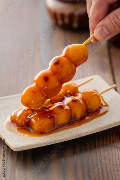 Fototapeta A close-up of traditional Japanese mitarashi dango—skewered rice dumplings grilled to perfection and coated with a glossy, sweet soy sauce glaze. The caramelized surface and rich glaze highlight the a
