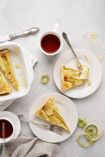Obraz A slices of rhubarb pie or tart on a white plates with cups of tea. summer breakfast concept .Tart with sour cream filling . Healthy homemade summer dessert, Top view, copy space.