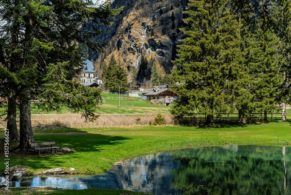 Fototapeta Alpine lake Gover surrounded by green trees as a mountain with a waterfall in the background in Gressoney Saint Jean, Italy.